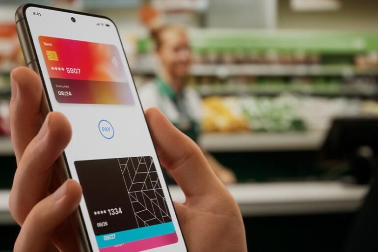 Person holding smartphone with digital wallet app displaying two credit cards in a grocery store checkout setting.