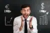 A man in a white shirt and tie looks excited, holding glasses. Behind him is a blackboard with chalk drawings of currency symbols and rising graphs.