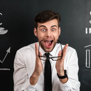 A man in a white shirt and tie looks excited, holding glasses. Behind him is a blackboard with chalk drawings of currency symbols and rising graphs.