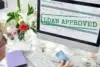 Computer screen showing an application form with "LOAN APPROVED" in bold green letters. Nearby, a person holds a credit card, with flowers on the desk.