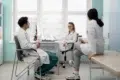 Three medical professionals in white coats have a relaxed discussion in a bright office. They appear engaged, conveying a collaborative atmosphere.