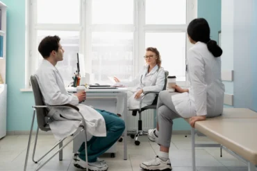 Three medical professionals in white coats have a relaxed discussion in a bright office. They appear engaged, conveying a collaborative atmosphere.