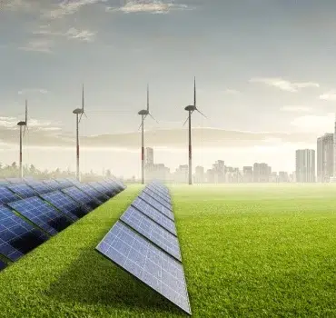A field of solar panels and wind turbines stand on a grassy plain, with a city skyline in the background under a bright, partly cloudy sky.