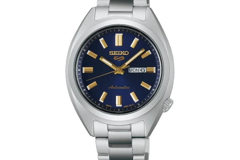 A silver metal Seiko watch with a blue dial, gold hour markers, and hands, displaying the day and date. The tone is elegant and sophisticated.