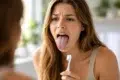 Person looking in mirror at white tongue even after brushing teeth