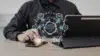 Person using a smartphone and tablet with digital cloud computing and data network icons floating above the devices on a wooden table.