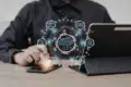 Person using a smartphone and tablet with digital cloud computing and data network icons floating above the devices on a wooden table.
