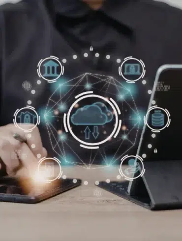 Person using a smartphone and tablet with digital cloud computing and data network icons floating above the devices on a wooden table.