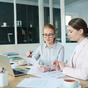 Two professional women review financial documents and a laptop in a modern office, representing the expert services provided by Accounting Companies in Abu Dhabi.