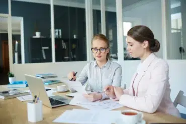 Two professional women review financial documents and a laptop in a modern office, representing the expert services provided by Accounting Companies in Abu Dhabi.