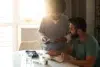 Healthcare professional explains medication to seated man at a sunlit table with medical supplies and notes.