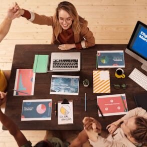 Overhead view of a diverse team celebrating around a desk with laptops and digital marketing materials, conveying teamwork and success.