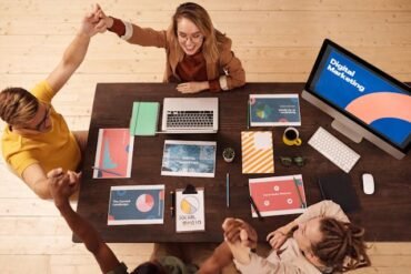 Overhead view of a diverse team celebrating around a desk with laptops and digital marketing materials, conveying teamwork and success.