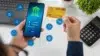 Person using mobile banking app on smartphone while holding a credit card, with digital finance icons floating nearby.