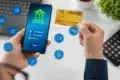 Person using mobile banking app on smartphone while holding a credit card, with digital finance icons floating nearby.