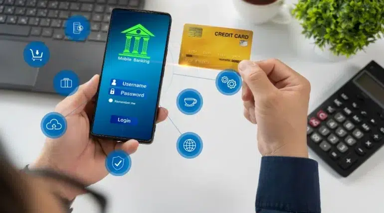 Person using mobile banking app on smartphone while holding a credit card, with digital finance icons floating nearby.