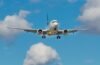 A silver airplane with blue accents is in flight against a vibrant blue sky dotted with white, fluffy clouds, conveying a sense of travel and freedom.