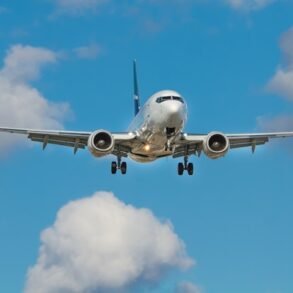 A silver airplane with blue accents is in flight against a vibrant blue sky dotted with white, fluffy clouds, conveying a sense of travel and freedom.