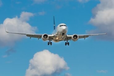 A silver airplane with blue accents is in flight against a vibrant blue sky dotted with white, fluffy clouds, conveying a sense of travel and freedom.