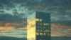 A modern glass skyscraper reflects a dramatic sunset with golden and orange hues against a cloudy sky, creating a serene and majestic atmosphere.