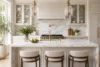 Spacious kitchen with marble countertops and island, featuring three cushioned stools, gold fixtures, pendant lights, and greenery, creating an elegant, airy feel.