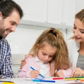 Singleton preschool learning moment with parents helping a young child draw and practice creativity at home