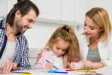 Singleton preschool learning moment with parents helping a young child draw and practice creativity at home