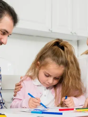 Singleton preschool learning moment with parents helping a young child draw and practice creativity at home