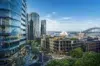 A vibrant cityscape featuring modern glass buildings, a lush rooftop garden, Sydney Opera House, and the Harbour Bridge under a clear blue sky.