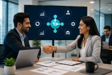 Two business professionals shake hands in an office, smiling. A digital presentation screen shows various business icons. Teamwork and success theme.