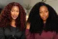 Two women with voluminous curly hair, one with dark red curls and the other with black curls, indoors with a neutral background.