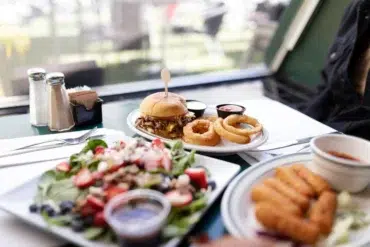 A table with a gourmet burger and onion rings, fresh salad with berries, and a plate of crispy mozzarella sticks, evoking a casual dining atmosphere.