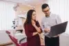 Two healthcare professionals reviewing information on a laptop in a dental clinic with equipment in the background.