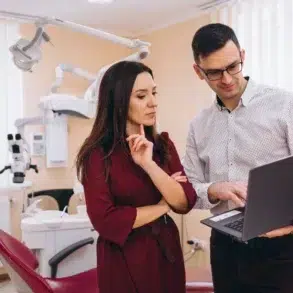 Two healthcare professionals reviewing information on a laptop in a dental clinic with equipment in the background.