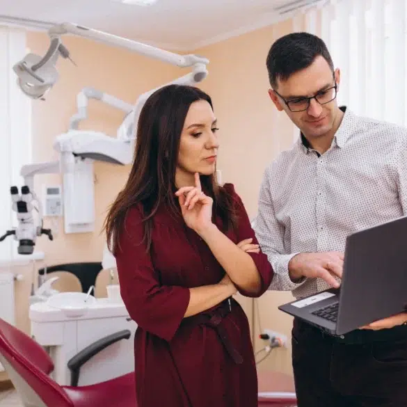 Two healthcare professionals reviewing information on a laptop in a dental clinic with equipment in the background.