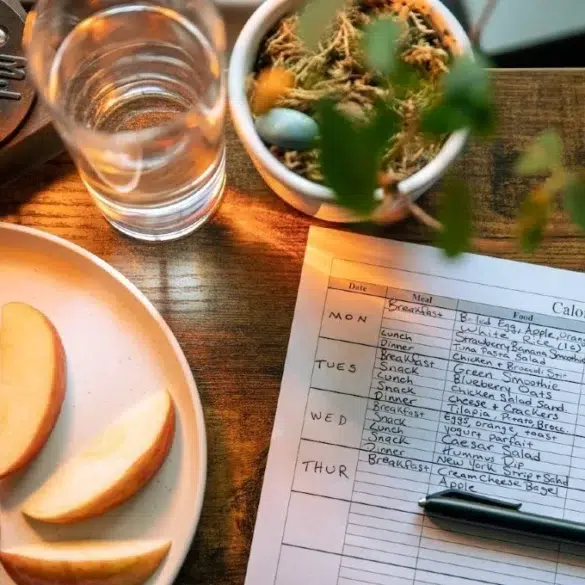 Apple slices on a plate, a glass of water, and a calorie counter sheet on a wood table, creating a health-focused, organized atmosphere.