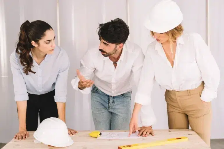 Office Renovation Builders in Sydney discussing plans over a table with blueprints and safety helmets during a project meeting.