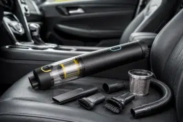 A sleek, portable vacuum cleaner with attachments is arranged on a car seat. The modern design conveys functionality and convenience.