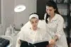 A woman in a spa chair reads a book, wearing a headband and robe, while another woman in a lab coat stands beside her, exuding a calm atmosphere.