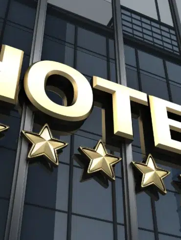 Gold "HOTEL" sign with five stars below, mounted on a reflective glass building facade. The image conveys luxury, elegance, and high-quality service.