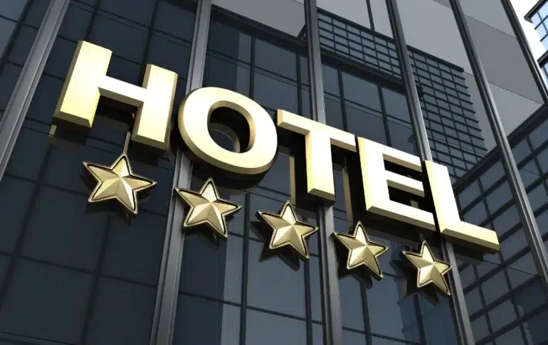 Gold "HOTEL" sign with five stars below, mounted on a reflective glass building facade. The image conveys luxury, elegance, and high-quality service.