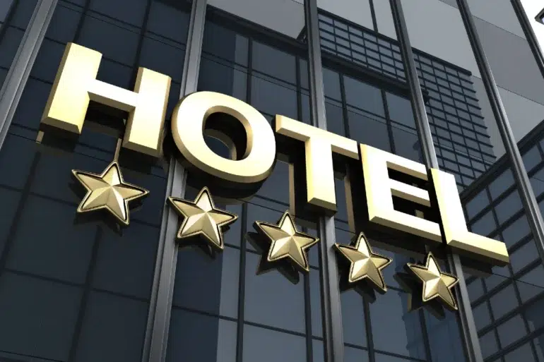 Gold "HOTEL" sign with five stars below, mounted on a reflective glass building facade. The image conveys luxury, elegance, and high-quality service.