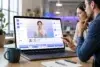 Two professionals review an AI-powered video editing interface on a laptop, showing a virtual presenter, timeline controls, and interactive training video elements in a modern office workspace.