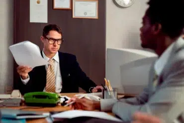 A Las Vegas Workers Comp Lawyer in a professional office setting, wearing glasses and a suit, reviewing legal documents during a consultation with a client.