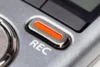 Close-up of a silver recording device with a prominent red REC button, symbolizing activation. The metallic texture adds a sleek, professional feel.