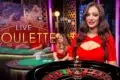 A smiling woman in a red dress stands beside a roulette table, exuding a lively casino atmosphere. The text "Live Roulette" is displayed prominently.