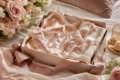 A beautifully arranged gift box contains satin lingerie in soft pink, adorned with lace. Nearby, blush roses and a silky ribbon add elegance and romance.