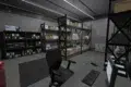 A tidy, well-lit storage room featuring shelves filled with organized boxes and folders. A desk with a computer, keyboard, and chair sits in the foreground.
