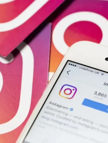 Close-up of a smartphone displaying Instagram's profile page, surrounded by cards featuring the Instagram logo on a gradient background. Social media theme.
