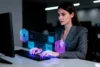 A woman in a suit works at a computer in a dimly lit office. Holographic blue and pink hexagons hover near her hands, suggesting digital interaction.
